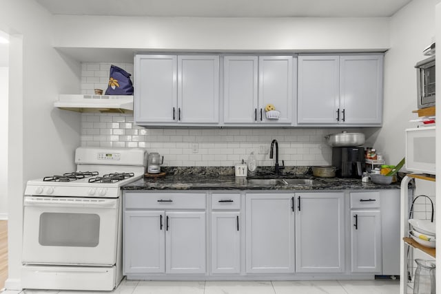 kitchen with dark stone counters, a sink, white gas range oven, under cabinet range hood, and tasteful backsplash