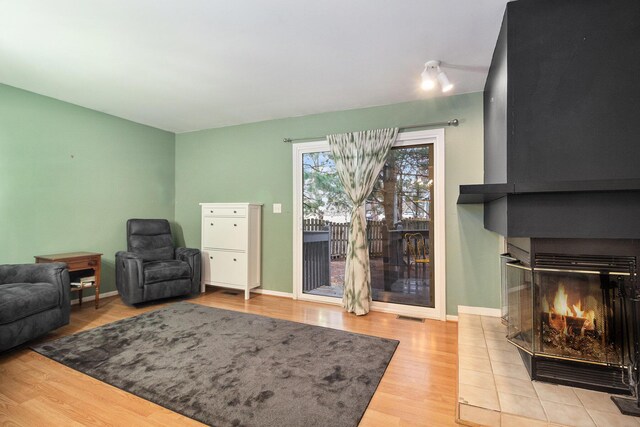 living area with baseboards, visible vents, wood finished floors, and a glass covered fireplace