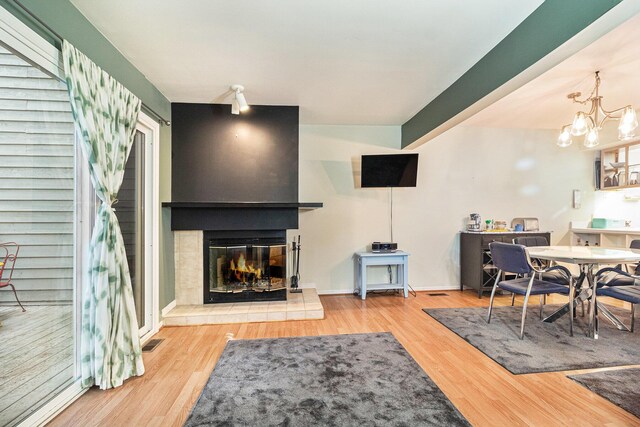 living area featuring visible vents, an inviting chandelier, a glass covered fireplace, wood finished floors, and baseboards