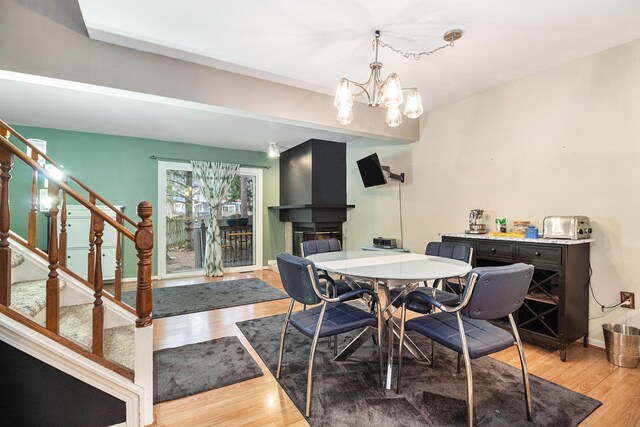 dining room featuring baseboards, a glass covered fireplace, wood finished floors, stairs, and a notable chandelier