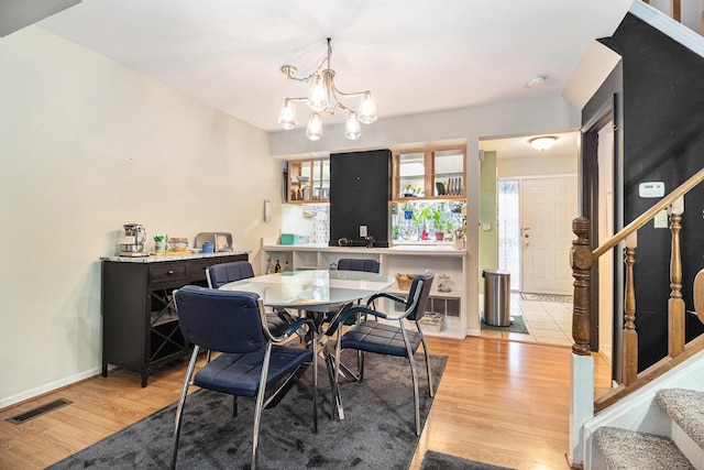 dining area featuring a chandelier, visible vents, light wood finished floors, and stairs