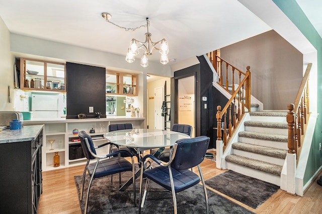 dining space with light wood-type flooring, an inviting chandelier, and stairway