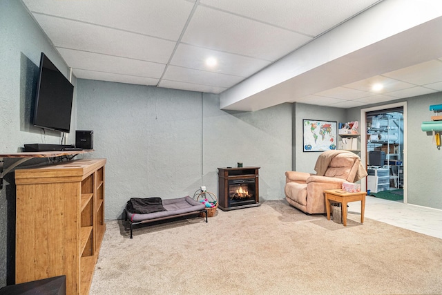 living area with carpet floors, a warm lit fireplace, a drop ceiling, and a textured wall