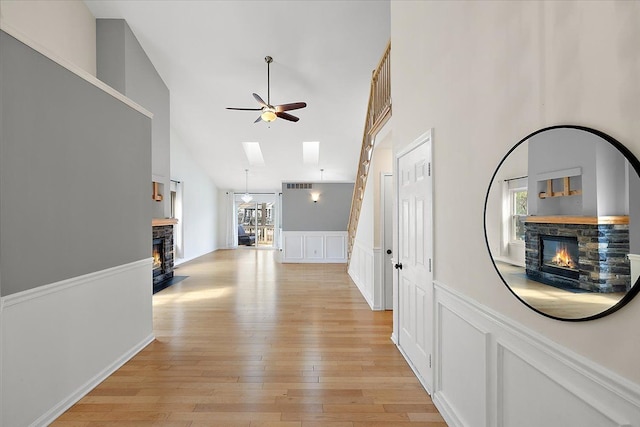 hallway featuring a skylight, a wainscoted wall, a decorative wall, light wood-style flooring, and a towering ceiling