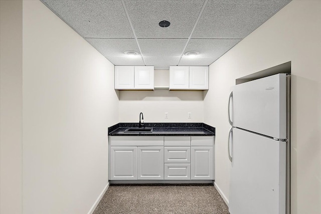 kitchen featuring white cabinets, a drop ceiling, freestanding refrigerator, dark colored carpet, and a sink