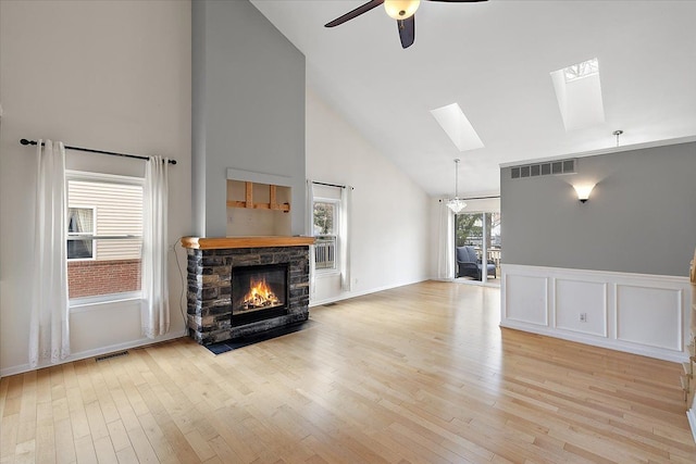 living room featuring a fireplace, a skylight, a ceiling fan, visible vents, and light wood-style floors