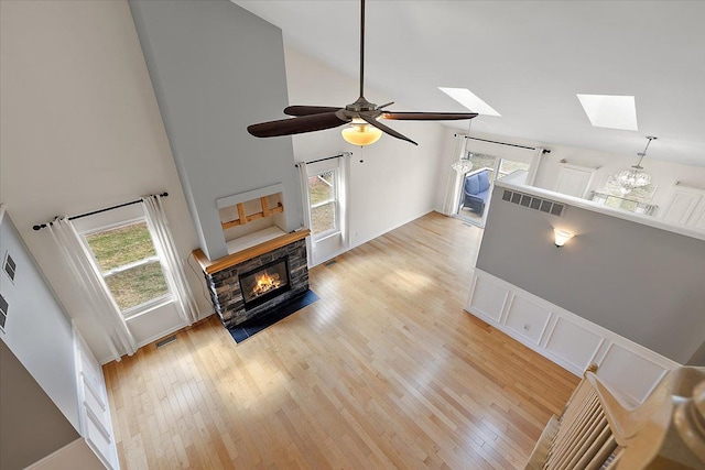 living area featuring a skylight, a fireplace, light wood finished floors, visible vents, and high vaulted ceiling