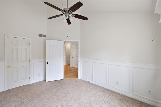 unfurnished bedroom featuring light colored carpet, wainscoting, visible vents, and ceiling fan