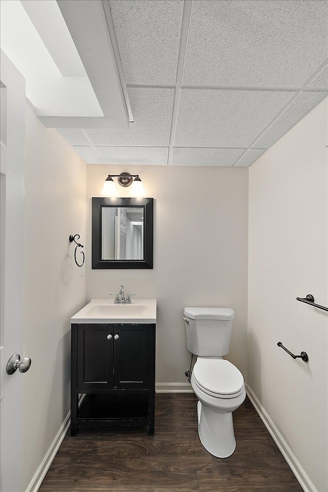 bathroom with a drop ceiling, toilet, wood finished floors, vanity, and baseboards