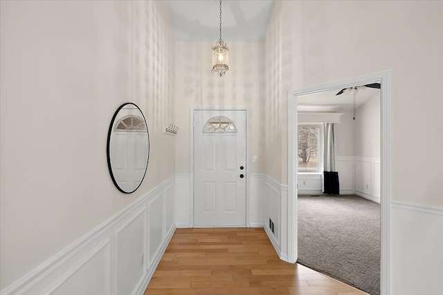 entryway featuring light carpet, wainscoting, a decorative wall, and light wood-style flooring