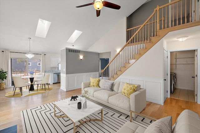 living room with a skylight, visible vents, light wood-style floors, stairs, and wainscoting