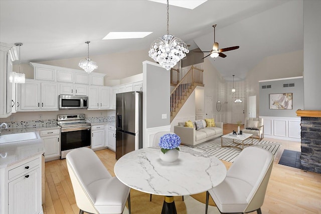 dining space with a decorative wall, ceiling fan with notable chandelier, a skylight, light wood-style floors, and stairs