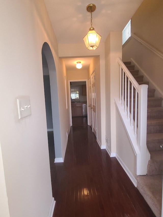 corridor with arched walkways, baseboards, stairway, and hardwood / wood-style floors