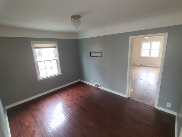 spare room with dark wood-style flooring, visible vents, and baseboards