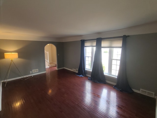 unfurnished room with baseboards, visible vents, arched walkways, and hardwood / wood-style floors