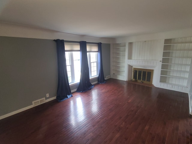 unfurnished living room featuring built in features, baseboards, visible vents, a glass covered fireplace, and wood finished floors