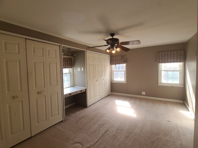 unfurnished bedroom with multiple windows, light carpet, baseboards, and two closets