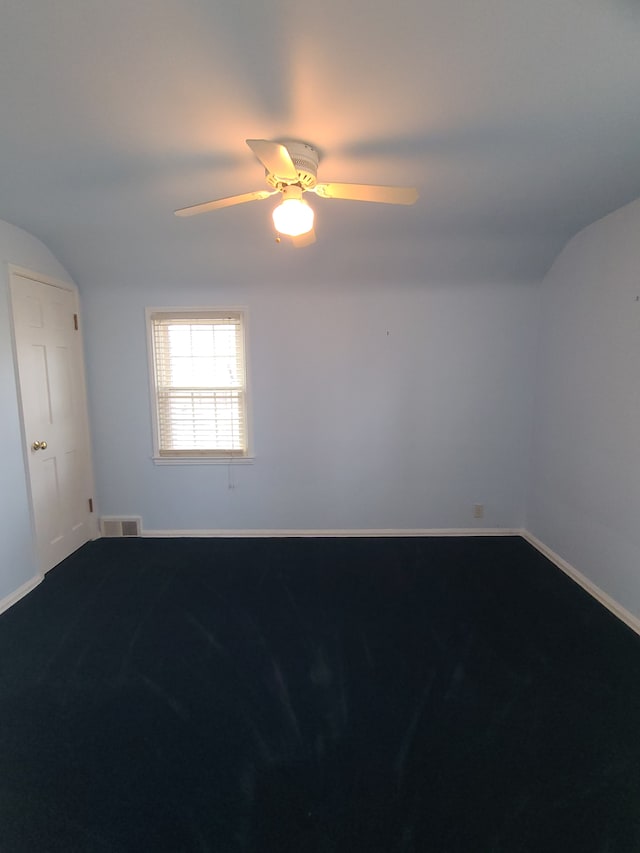 empty room with ceiling fan, visible vents, baseboards, vaulted ceiling, and dark colored carpet