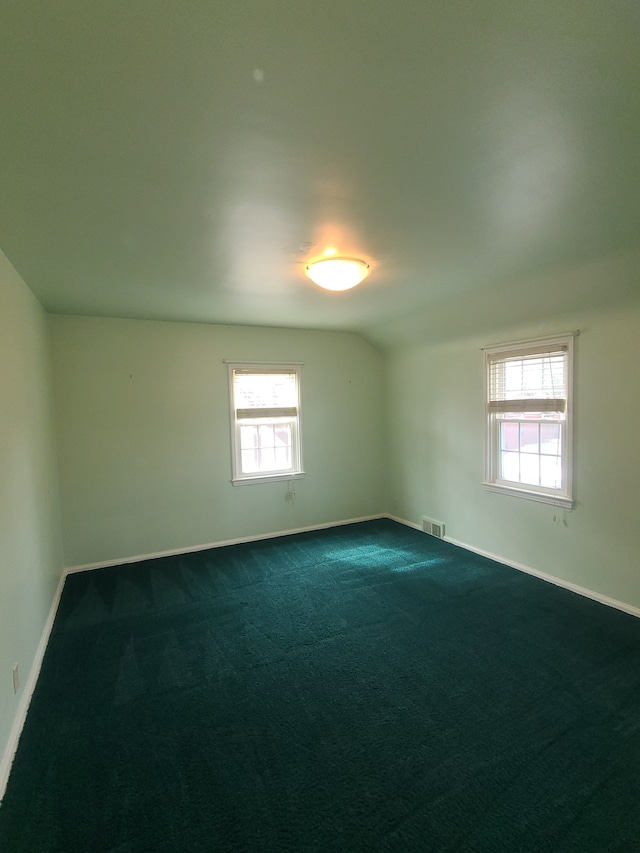 unfurnished room featuring vaulted ceiling, dark colored carpet, visible vents, and baseboards