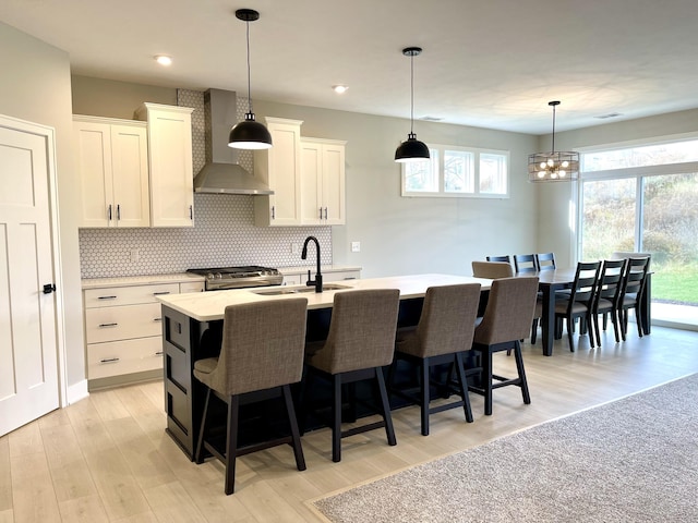 kitchen featuring light countertops, decorative backsplash, a sink, wall chimney range hood, and a kitchen bar