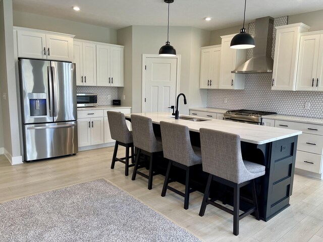 kitchen with stainless steel appliances, a sink, white cabinets, wall chimney range hood, and light wood-type flooring