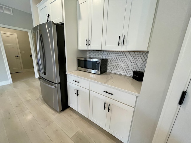 kitchen with tasteful backsplash, visible vents, light wood-style flooring, appliances with stainless steel finishes, and light stone counters