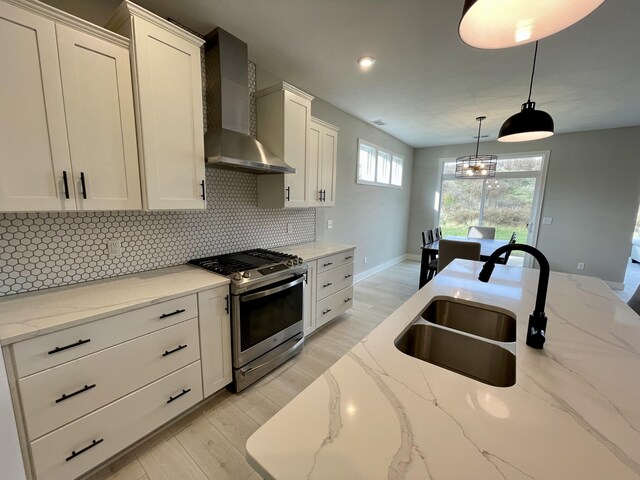 kitchen with a sink, white cabinetry, wall chimney range hood, backsplash, and gas range