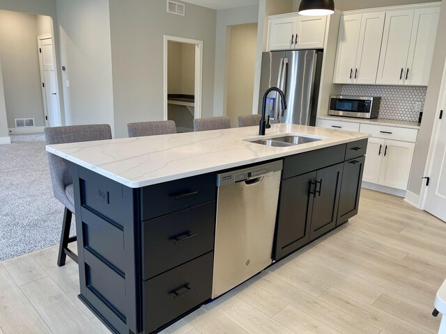 kitchen featuring a center island with sink, white cabinets, appliances with stainless steel finishes, a breakfast bar area, and a sink