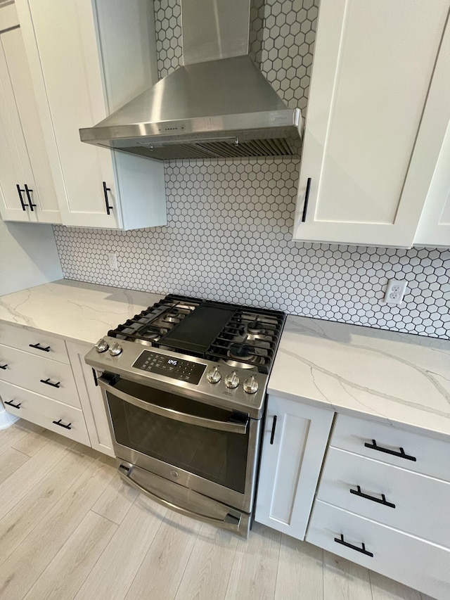 kitchen with white cabinetry, wall chimney range hood, light wood-type flooring, stainless steel range with gas cooktop, and tasteful backsplash