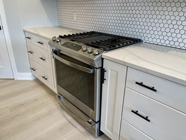 kitchen featuring light stone counters, white cabinetry, light wood-type flooring, backsplash, and stainless steel gas stove