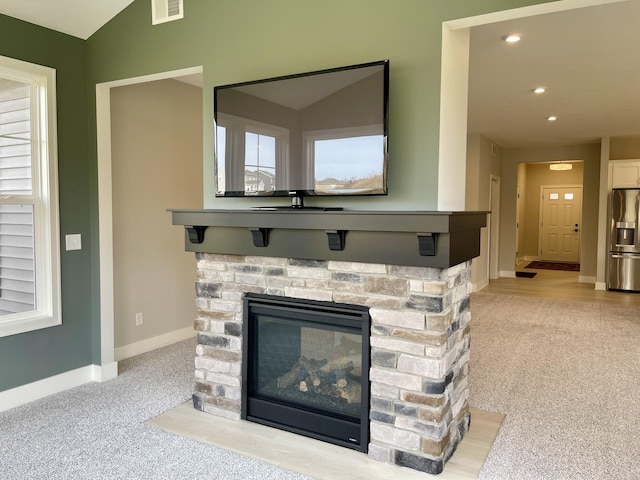 interior details with a stone fireplace, carpet floors, visible vents, baseboards, and stainless steel fridge with ice dispenser