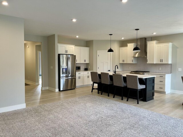 kitchen featuring tasteful backsplash, appliances with stainless steel finishes, a kitchen breakfast bar, wall chimney range hood, and white cabinetry