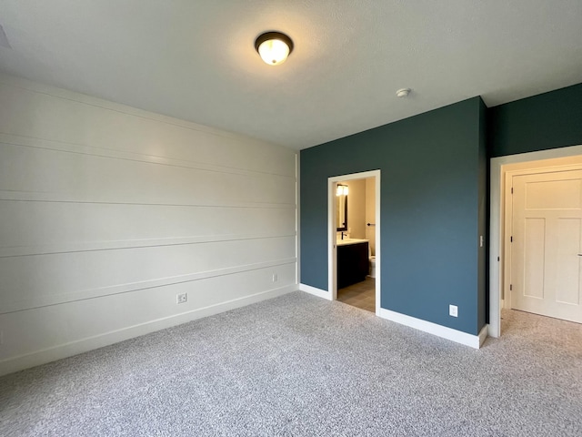 unfurnished bedroom featuring ensuite bath, baseboards, and carpet flooring