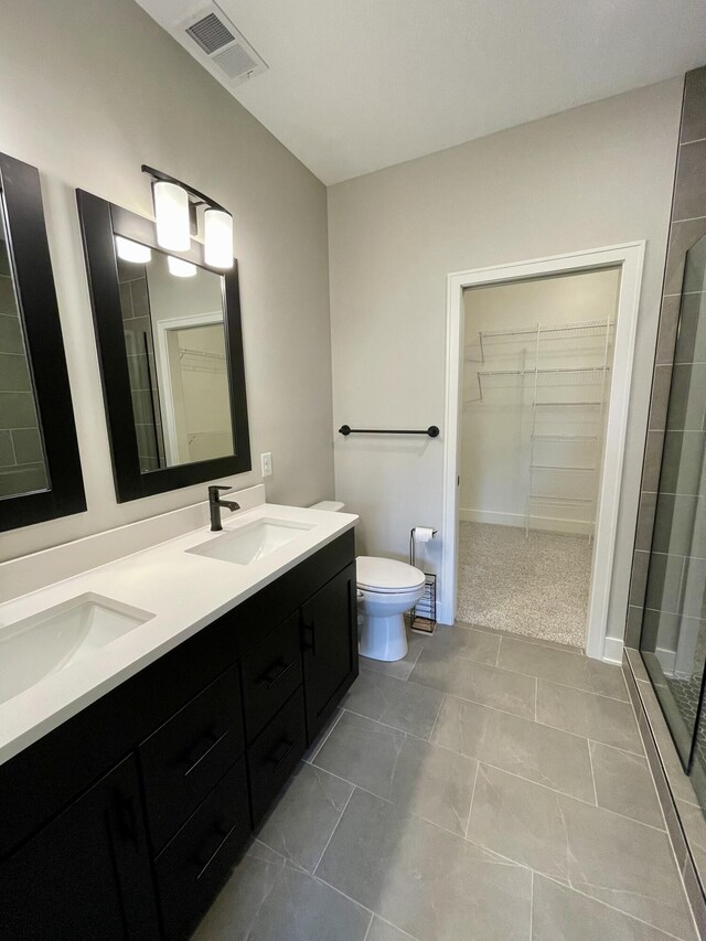 bathroom featuring visible vents, tiled shower, toilet, a walk in closet, and a sink