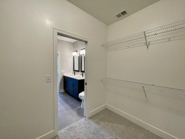 spacious closet featuring dark colored carpet, visible vents, and a sink