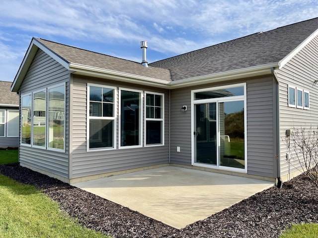 back of property with roof with shingles and a patio area