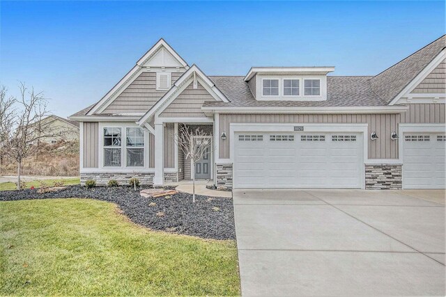 craftsman house featuring board and batten siding, a front yard, a garage, stone siding, and driveway