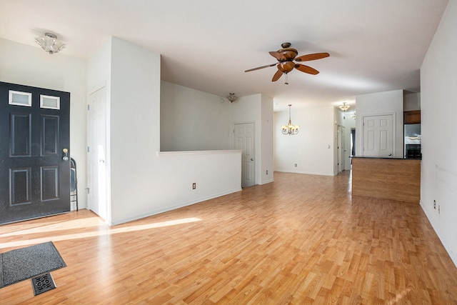 unfurnished living room featuring ceiling fan with notable chandelier, light wood-type flooring, and baseboards