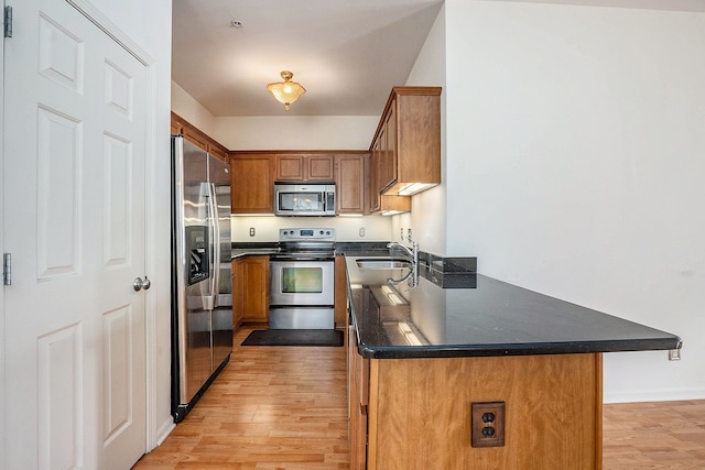 kitchen with light wood-type flooring, a sink, dark countertops, appliances with stainless steel finishes, and brown cabinetry