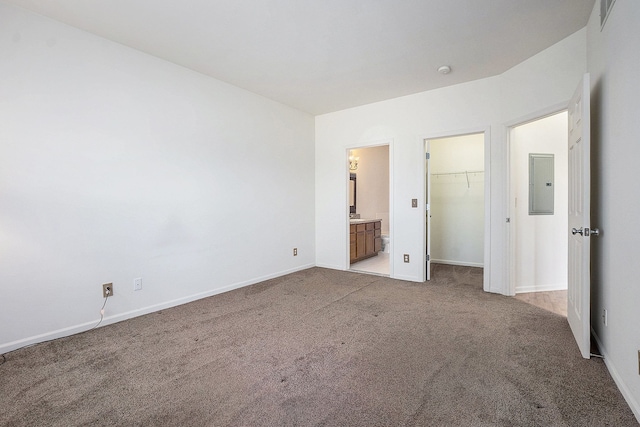 unfurnished bedroom with electric panel, a walk in closet, baseboards, and carpet flooring