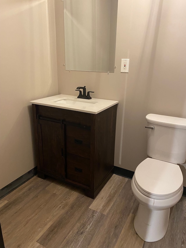 bathroom featuring baseboards, toilet, wood finished floors, and vanity