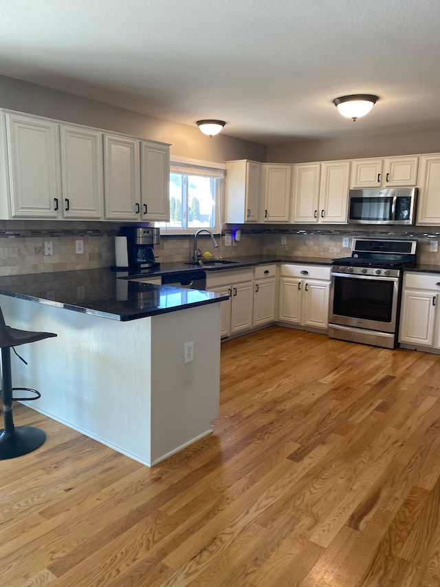 kitchen with a peninsula, light wood-style flooring, stainless steel appliances, white cabinets, and dark countertops