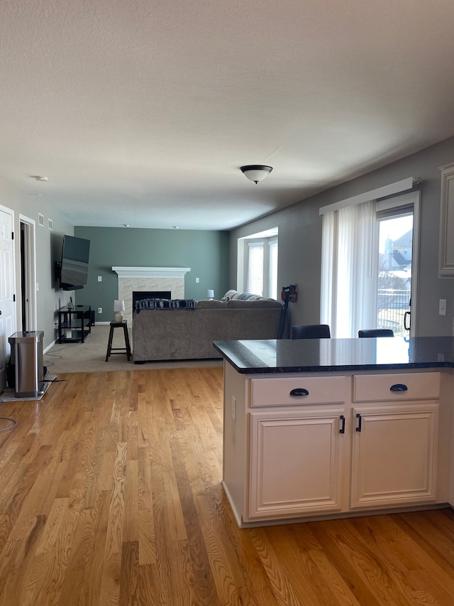 kitchen with dark countertops, baseboards, light wood-style flooring, a fireplace, and white cabinets