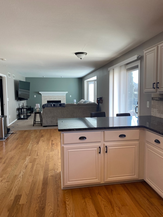 kitchen with light wood-style flooring, dark countertops, open floor plan, a peninsula, and a fireplace