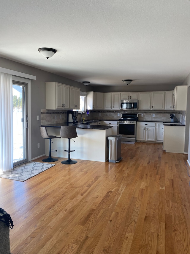 kitchen featuring dark countertops, tasteful backsplash, light wood-style floors, appliances with stainless steel finishes, and a healthy amount of sunlight