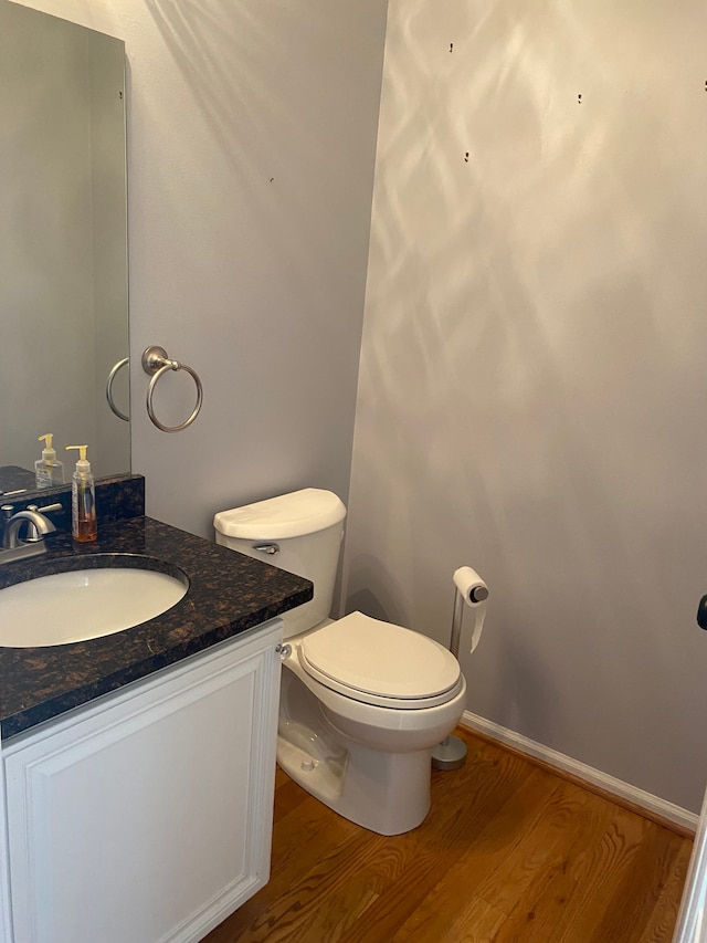 bathroom with toilet, vanity, baseboards, and wood finished floors