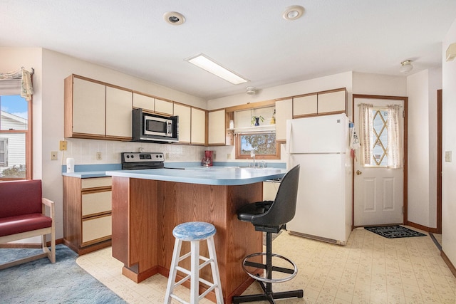 kitchen with baseboards, a kitchen island, a kitchen breakfast bar, stainless steel appliances, and light floors