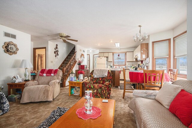 living room featuring stairway, ceiling fan with notable chandelier, visible vents, and light colored carpet