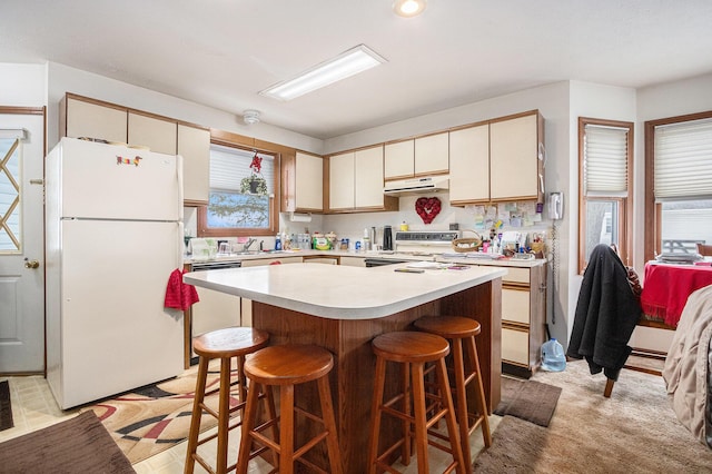 kitchen featuring a center island, light countertops, white appliances, under cabinet range hood, and a kitchen breakfast bar