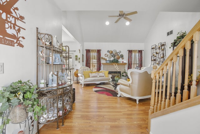 living room featuring visible vents, a tiled fireplace, stairs, wood finished floors, and a ceiling fan